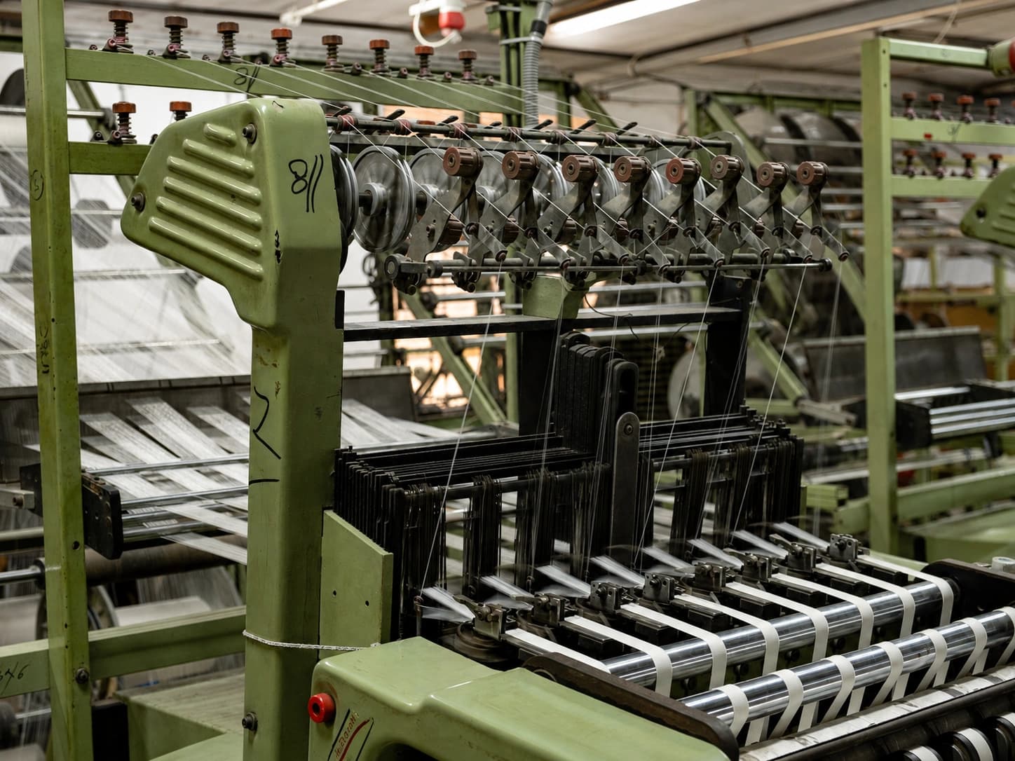 Close view of a narrow-fabric loom, woven tape emerging from the reed