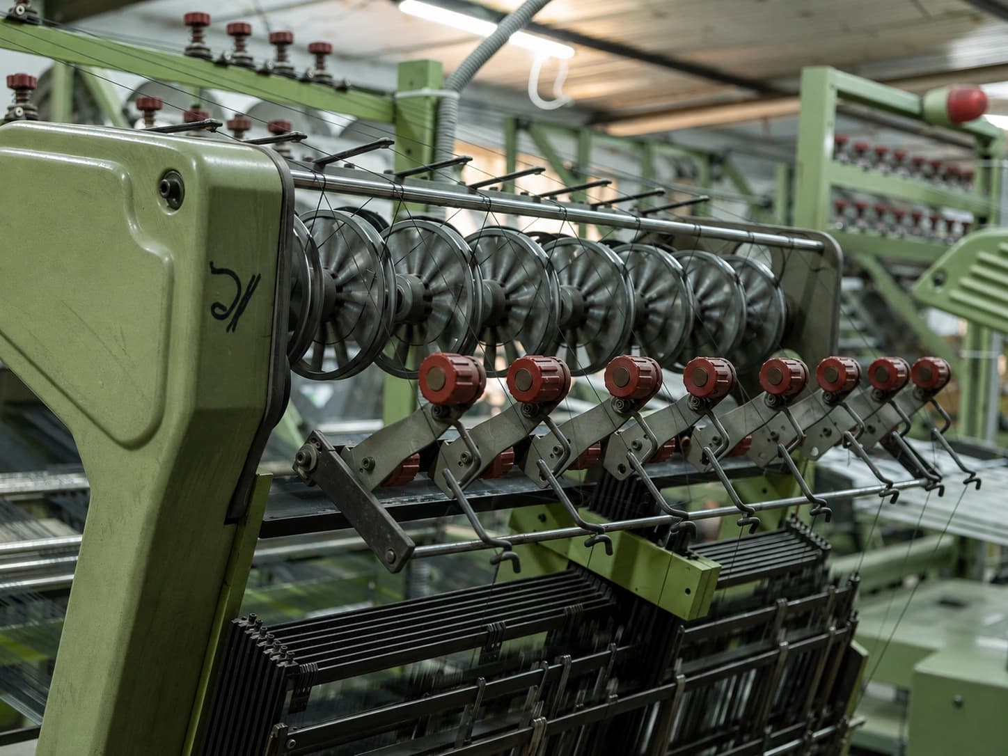 Close view of a narrow-fabric loom, a bank of thread spools feeding the machine