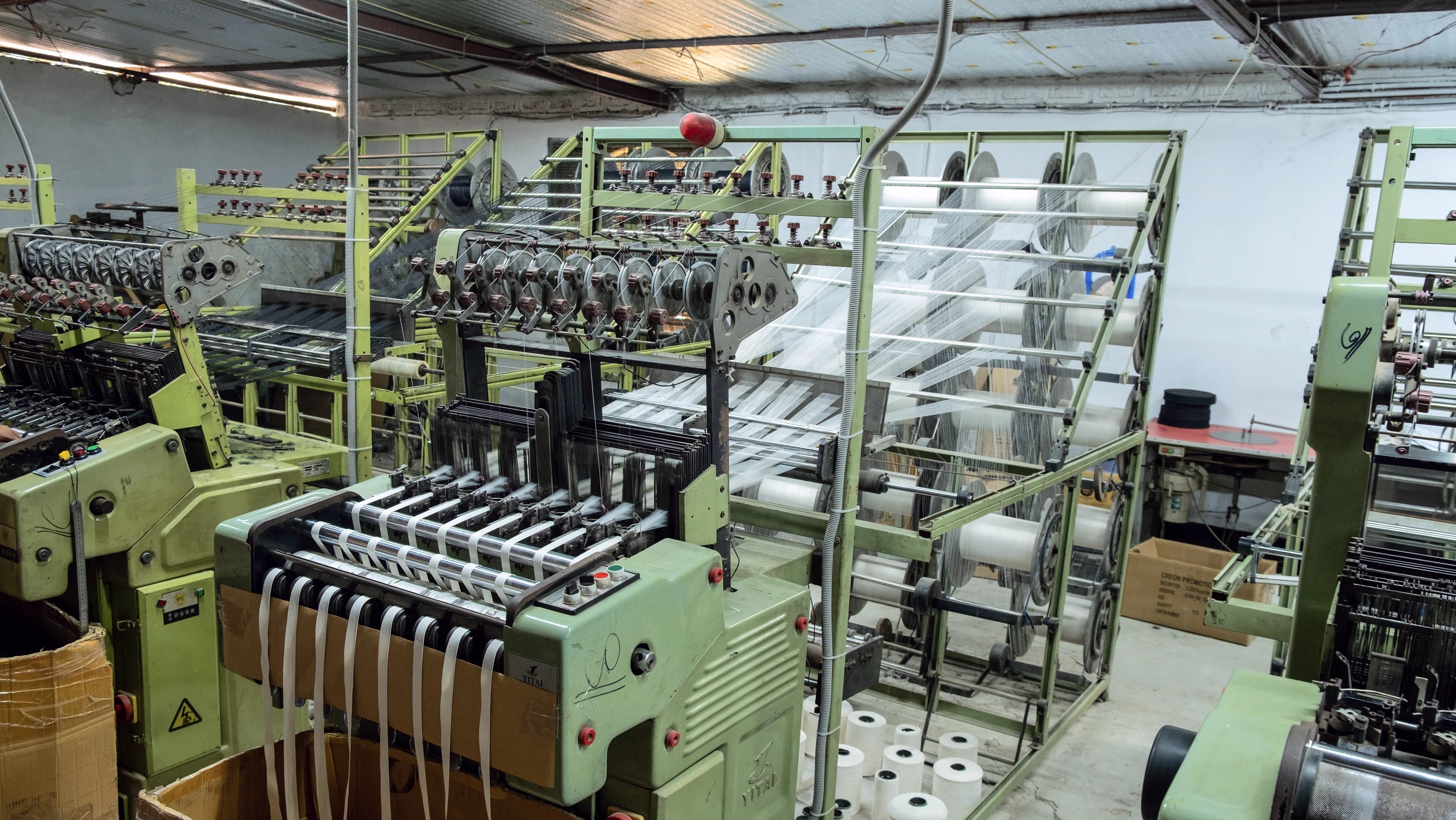 Wide view of the narrow-fabric weaving floor, rows of looms running the length of the hall