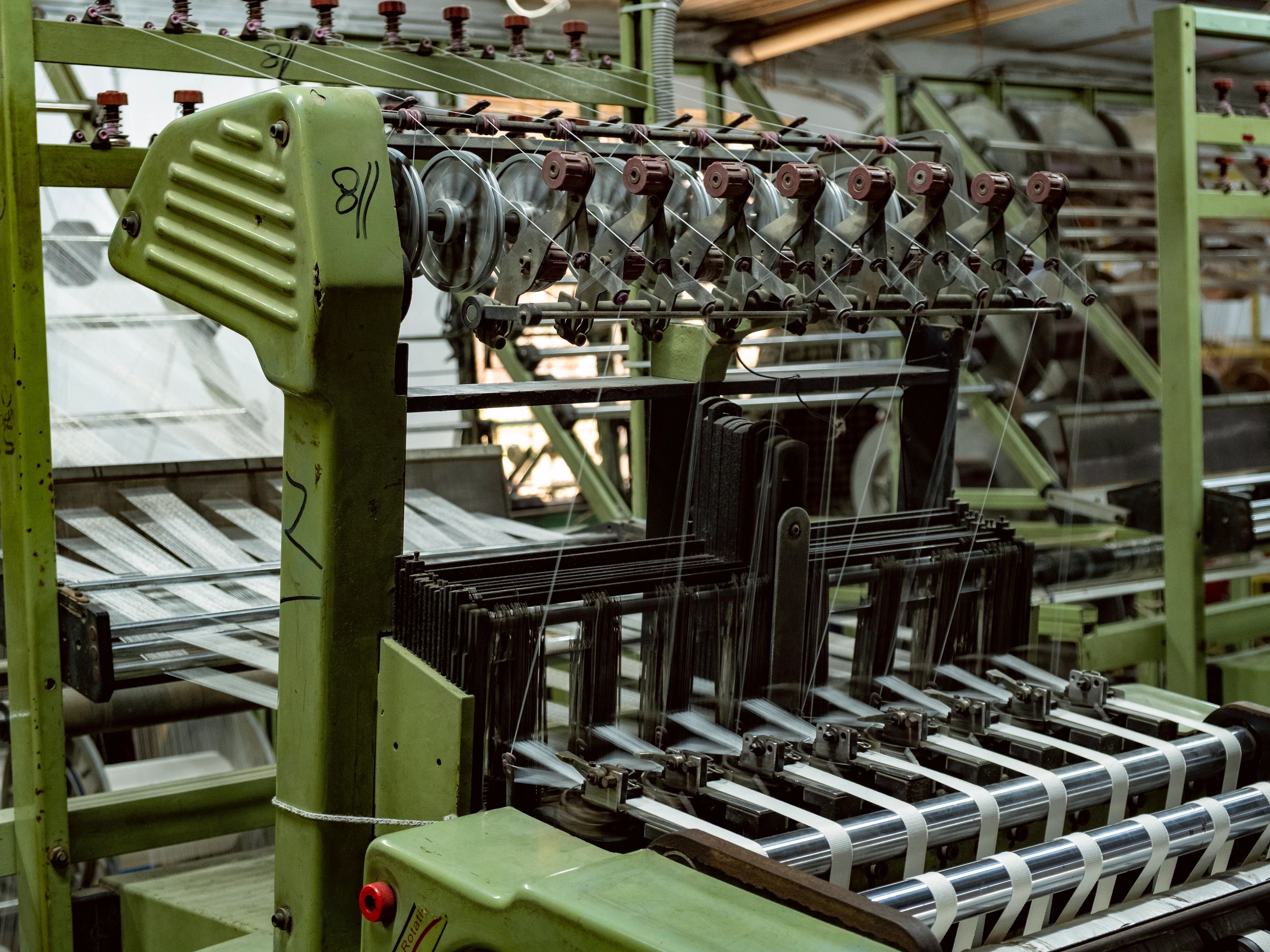 Close view of a narrow-fabric loom, woven tape emerging from the reed