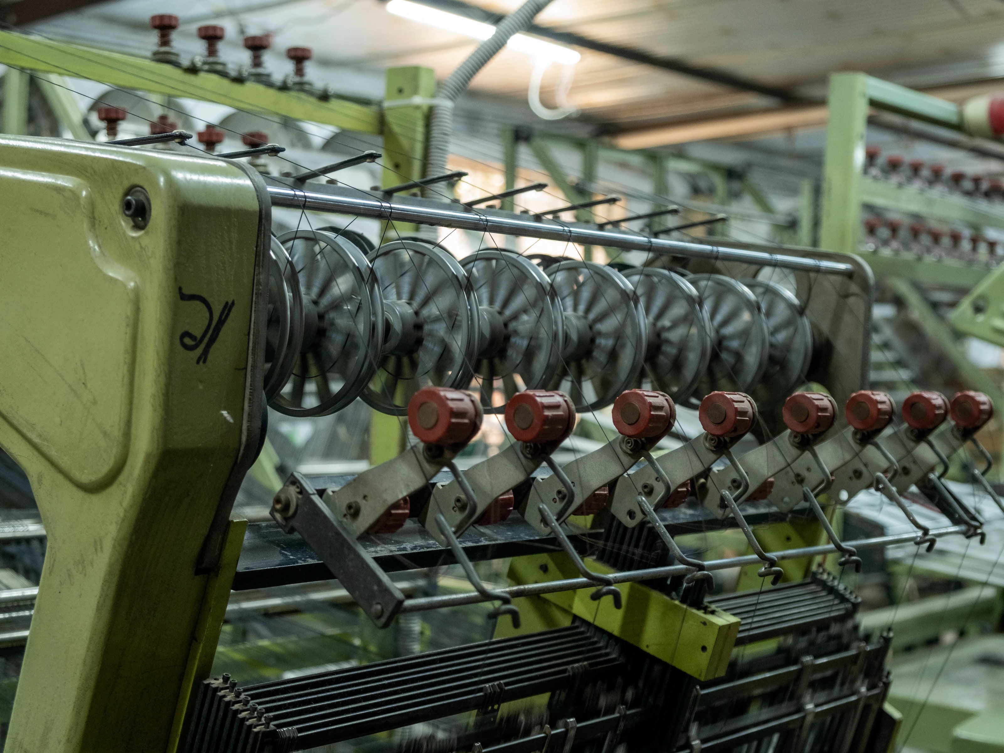 Close view of a narrow-fabric loom, a bank of thread spools feeding the machine