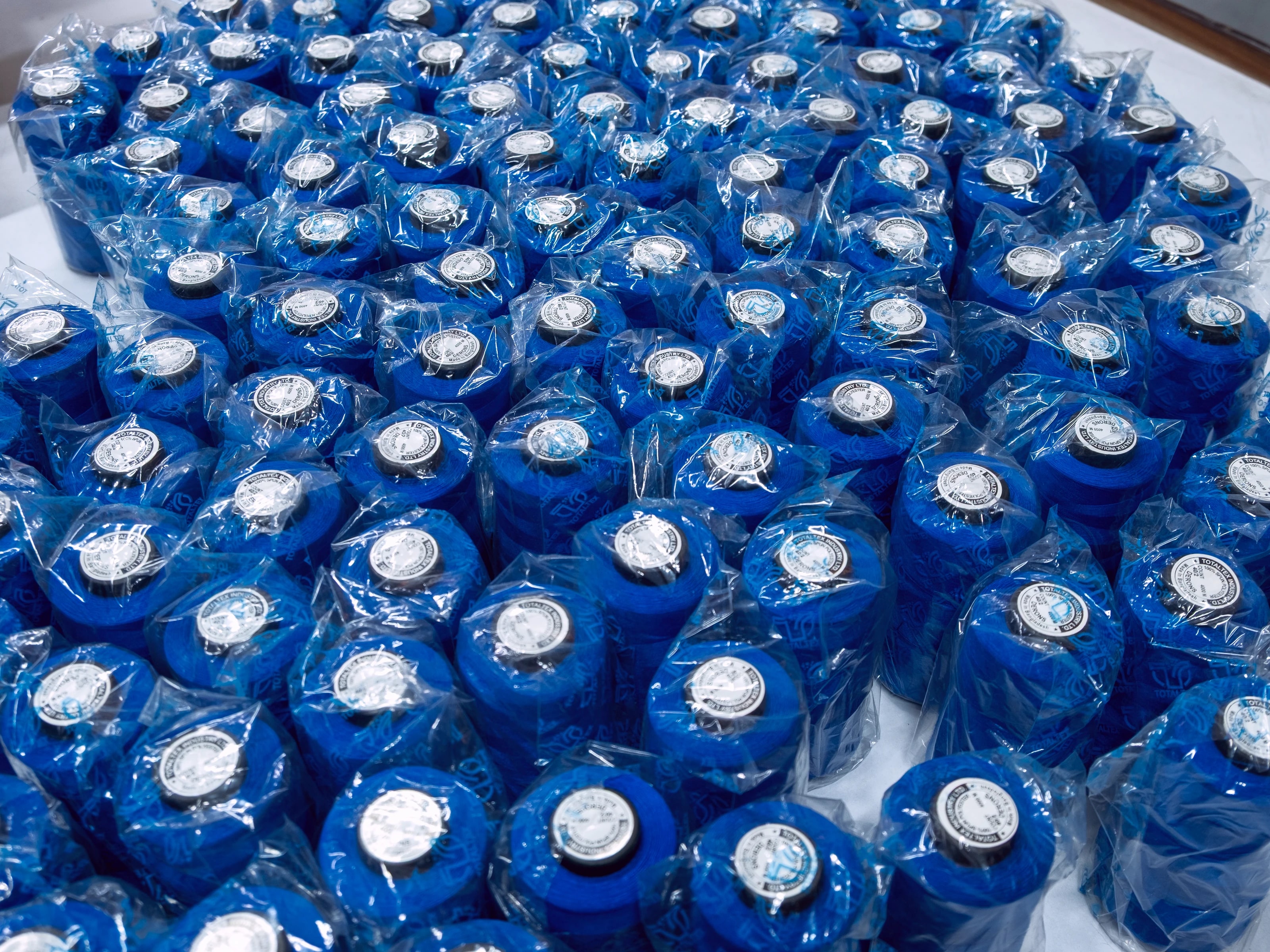 A mass of blue sewing thread cones packed in poly bags, seen from above