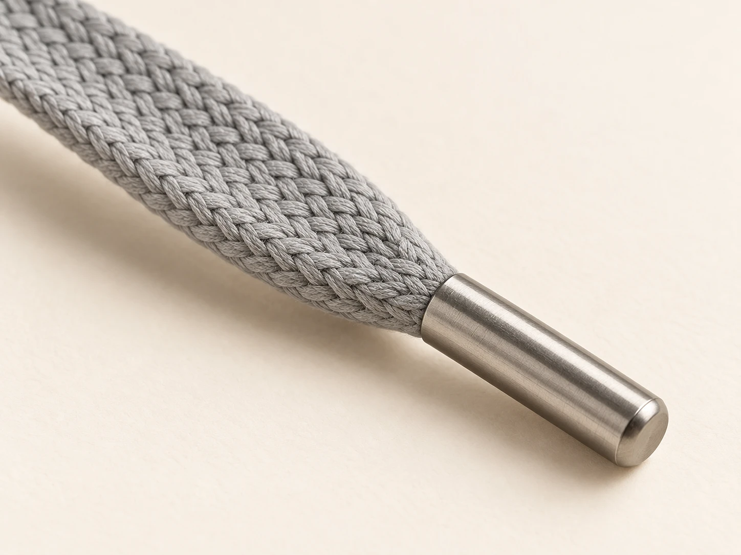 Close view of flat grey braided cord with a metal tip